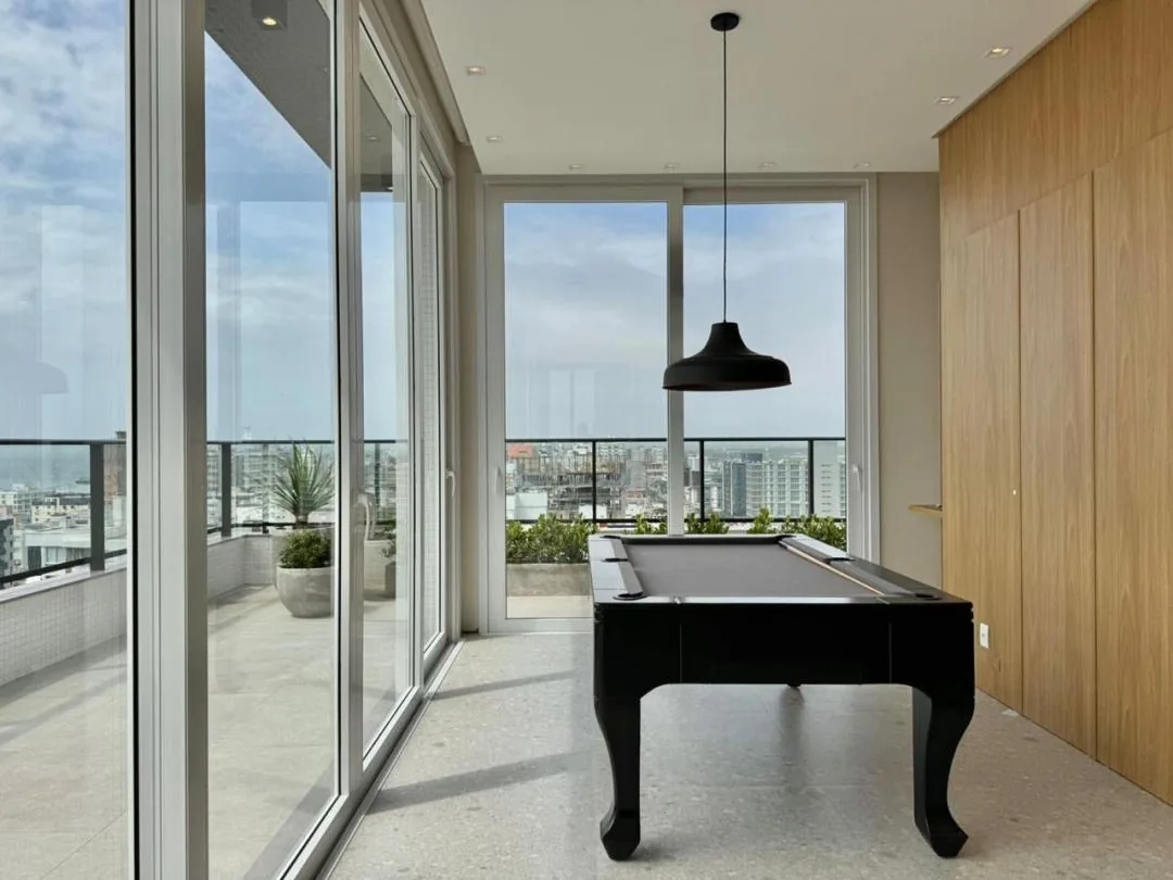 Salão com mesa de sinuca, luminária preta e painel de madeira.