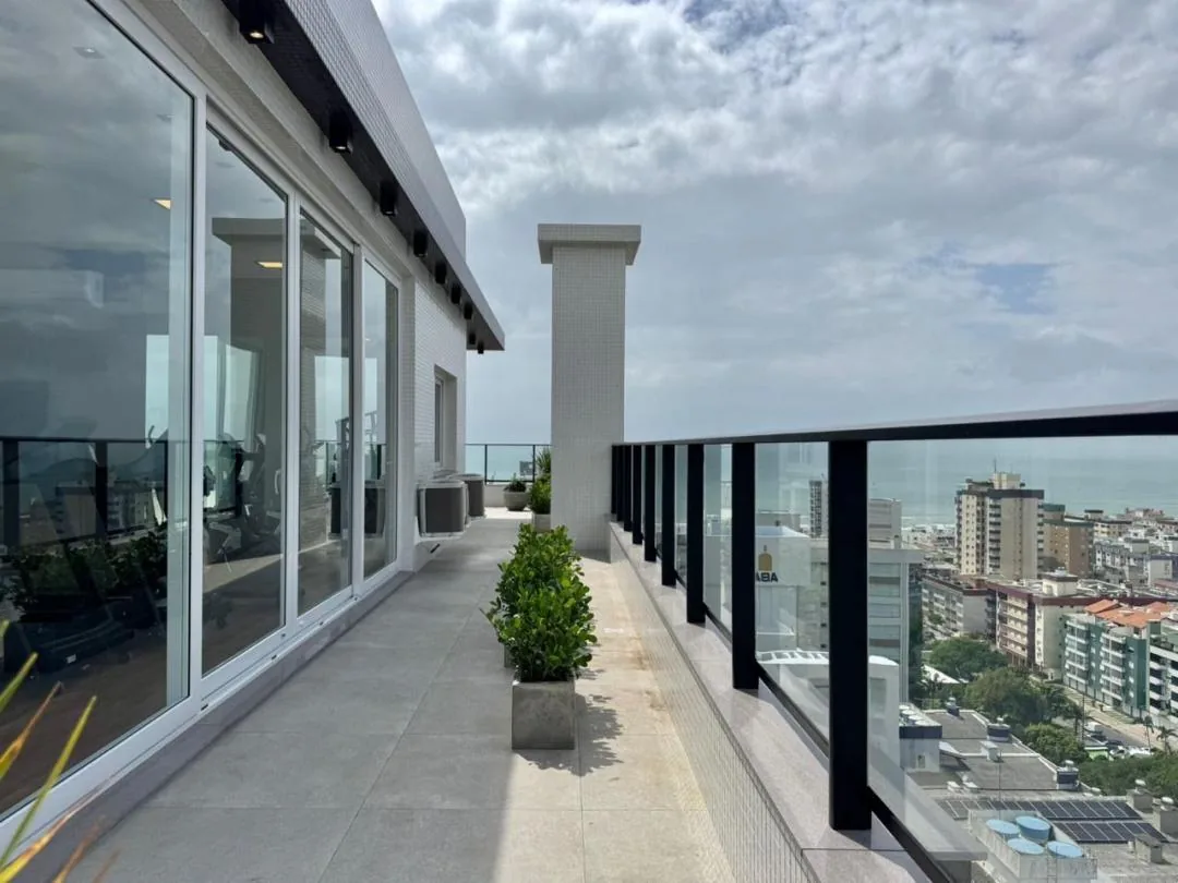 Corredor externo do rooftop com vasos e guarda-corpo de vidro.