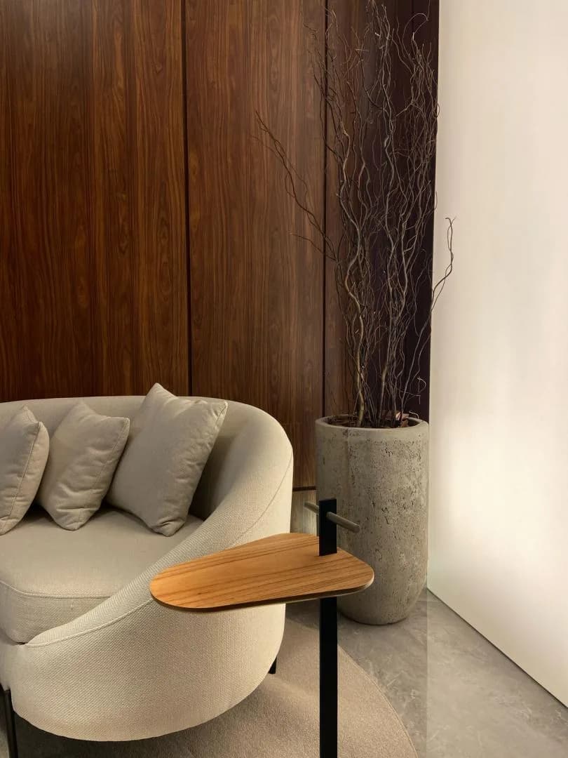 Poltrona curva bege com almofadas ao lado de vaso alto no hall.