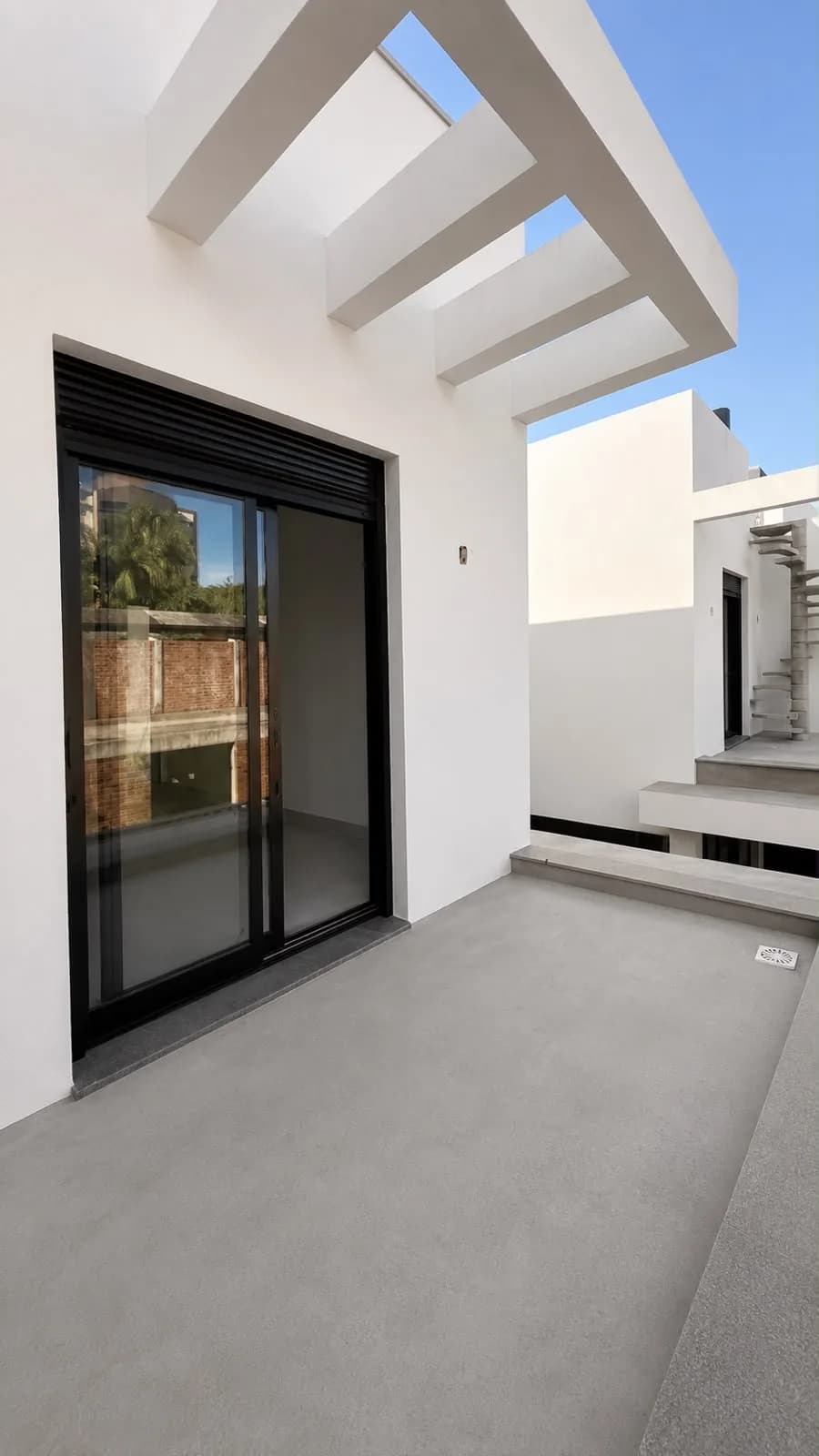 Terraço externo com pergolado de concreto e porta de correr.