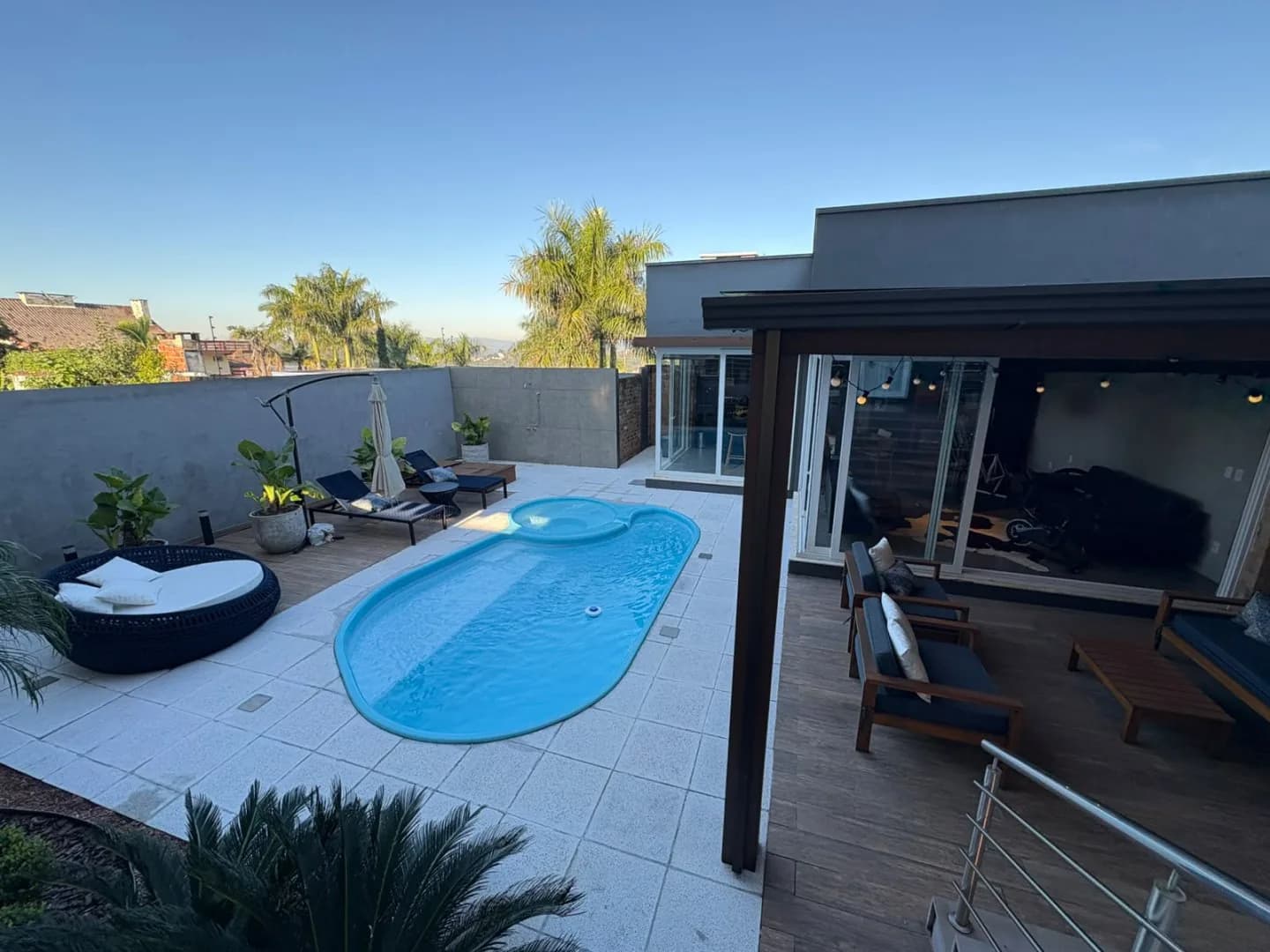 A casa contemporânea vista do pátio, com a piscina em primeiro plano e palmeiras ao fundo.