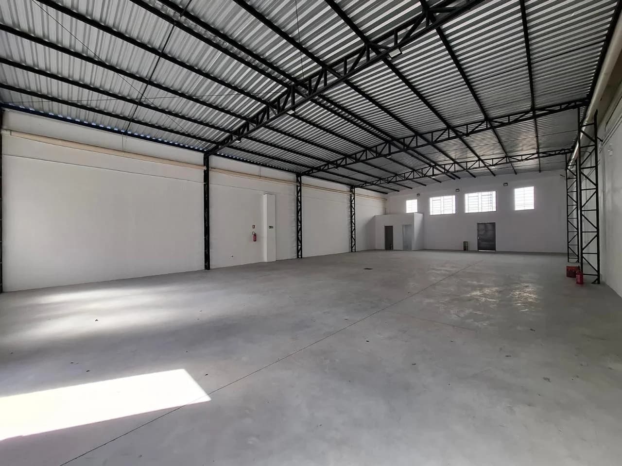 Interior do galpão vazio, piso de concreto e estrutura metálica aparente no telhado