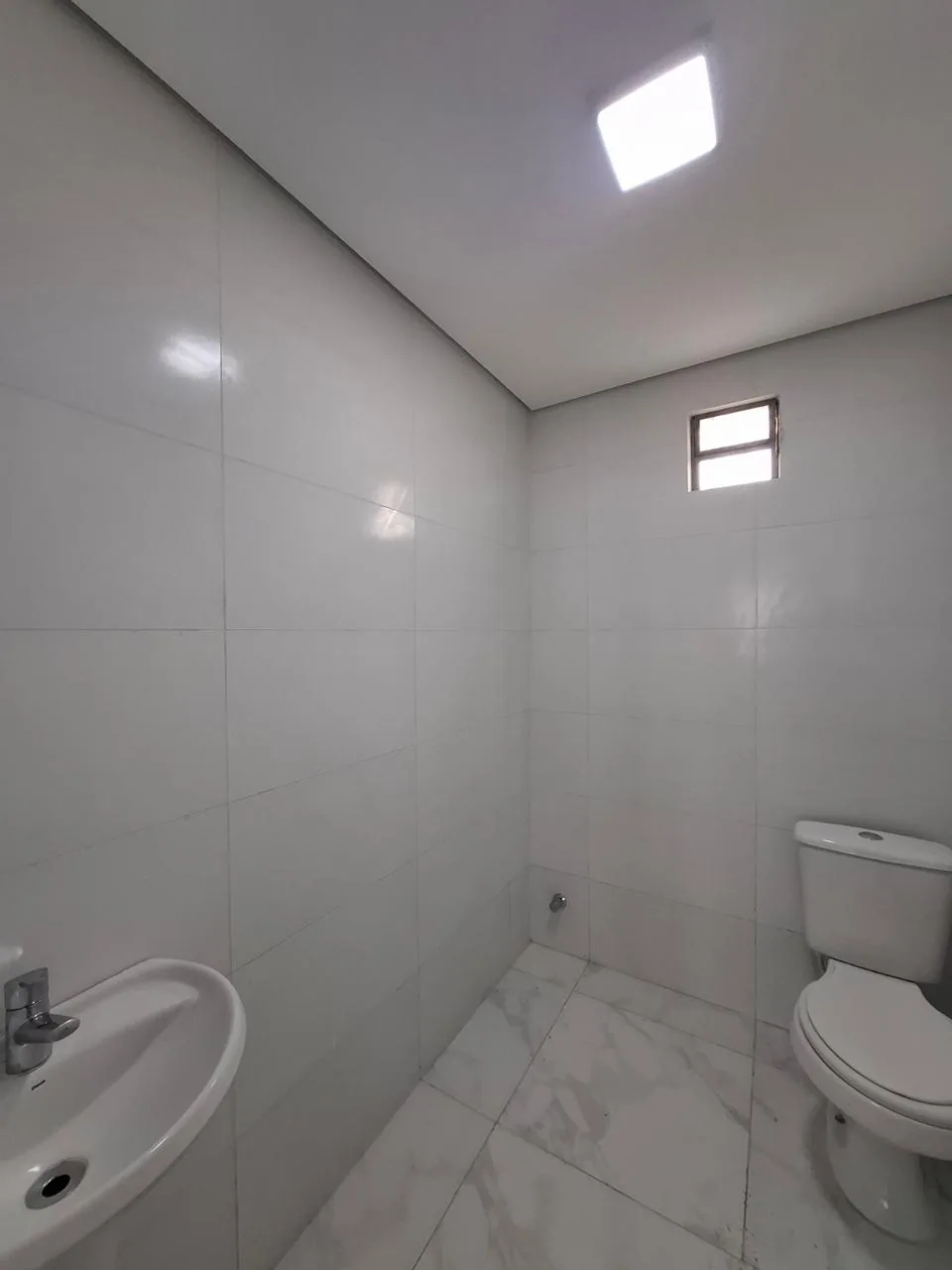Banheiro do pavilhão, com vaso sanitário branco e janela alta
