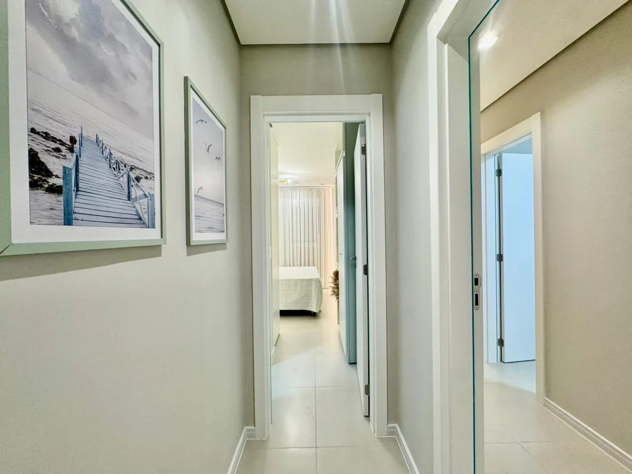Corredor com quadros de praia e porta aberta para um quarto ao fundo
