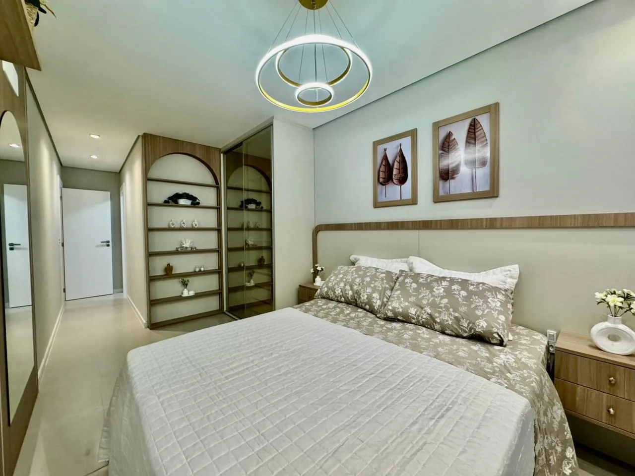 Suíte com cama de casal, lustre de anéis, estante em arco e armário com portas de vidro