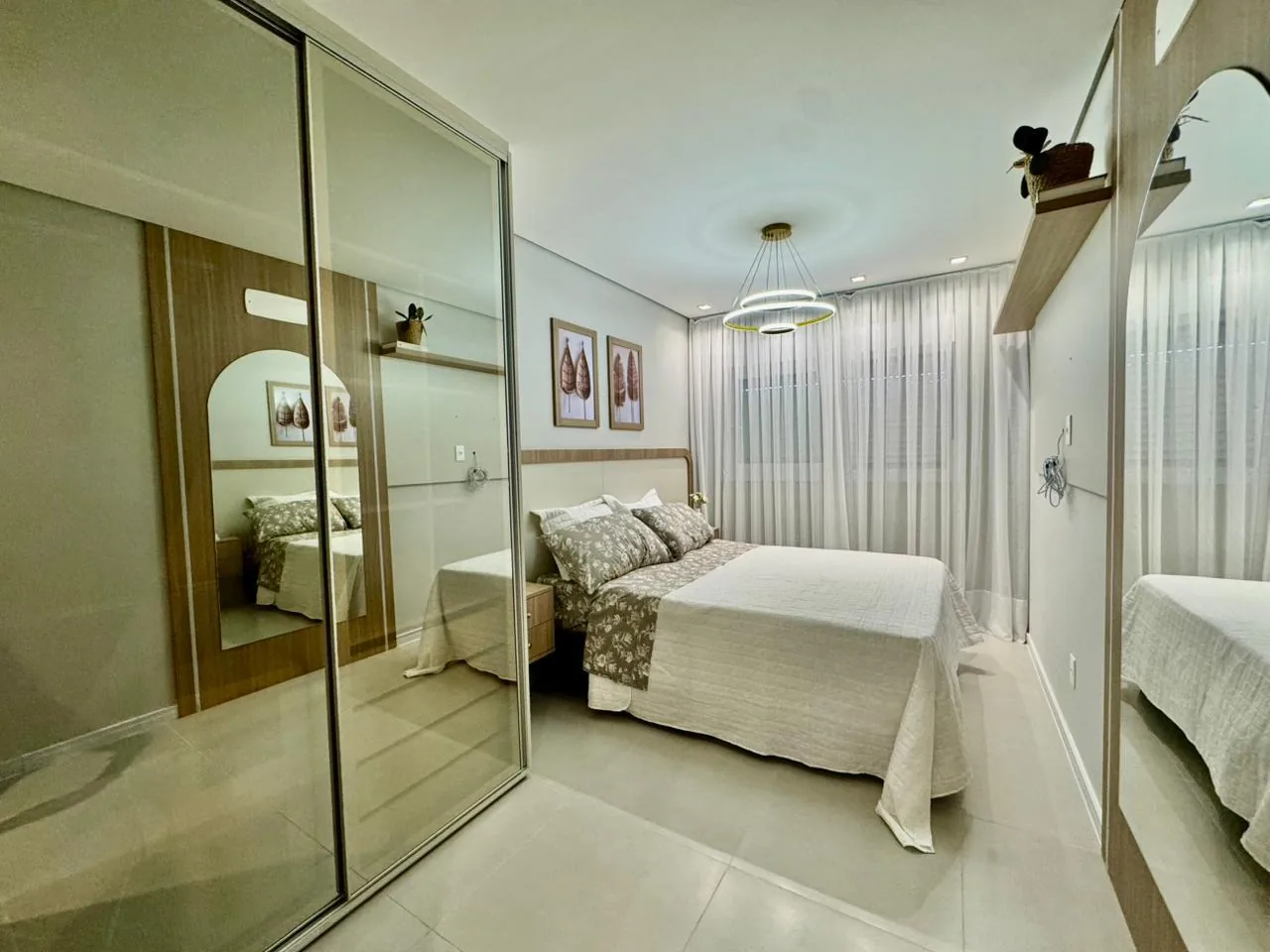 Suíte com armário de portas espelhadas, cama de casal com roupa de cama floral e cortinas claras