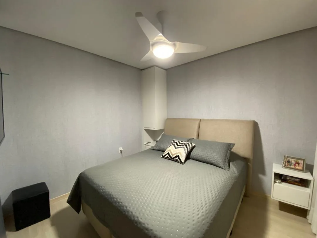 Quarto com cama de casal de colcha cinza, cabeceira estofada bege, papel de parede cinza e ventilador de teto