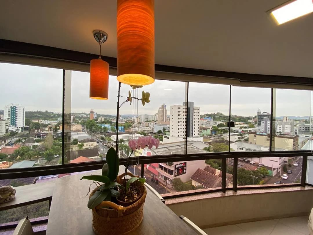 Sacada envidraçada com mesa, pendentes laranja e vista ampla da cidade do alto