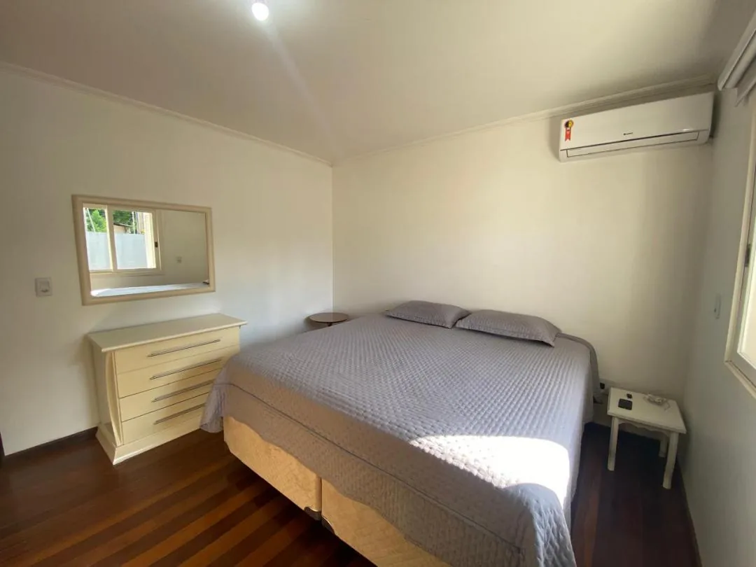 Quarto com cama de casal, cômoda clara com espelho, ar-condicionado split e piso de madeira