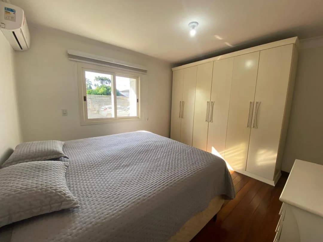 Quarto com cama de casal, roupeiro branco de portas altas e janela com persiana