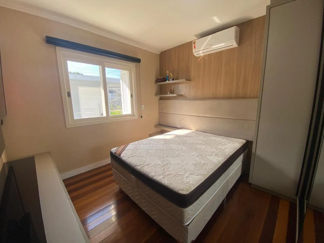 Quarto com painel amadeirado, cabeceira estofada, prateleiras e ar-condicionado split