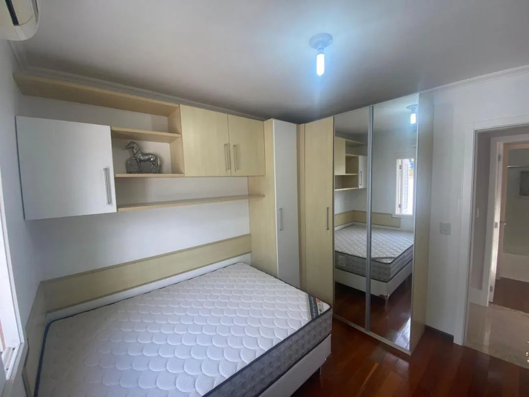 Quarto com armários aéreos planejados, roupeiro com portas espelhadas e piso de madeira