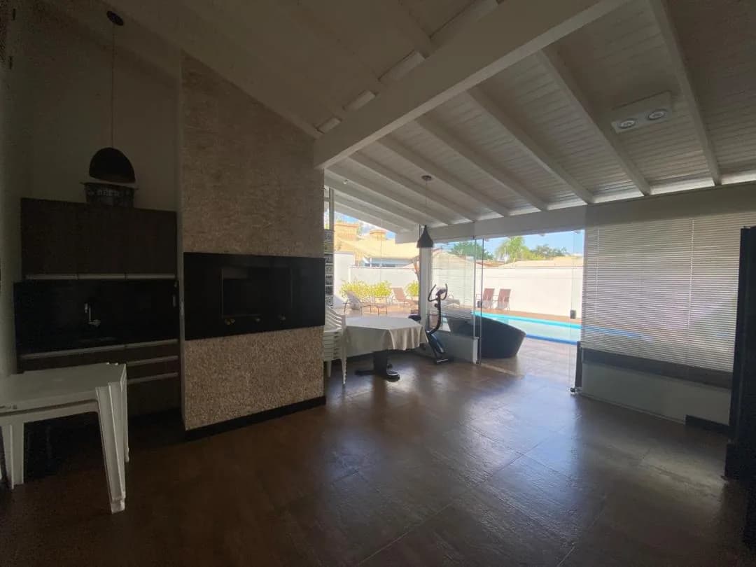 Espaço gourmet com churrasqueira revestida em pedra, armários escuros e portas de vidro abertas para a piscina