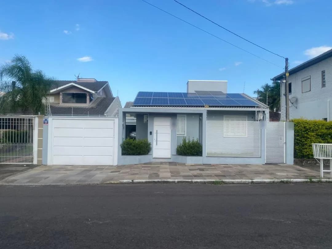 Fachada térrea com placas solares no telhado, portão de garagem branco e grade de lâminas horizontais