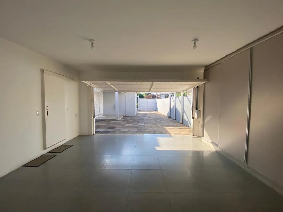 Garagem coberta com piso cerâmico cinza, armários embutidos na parede e saída para o pátio