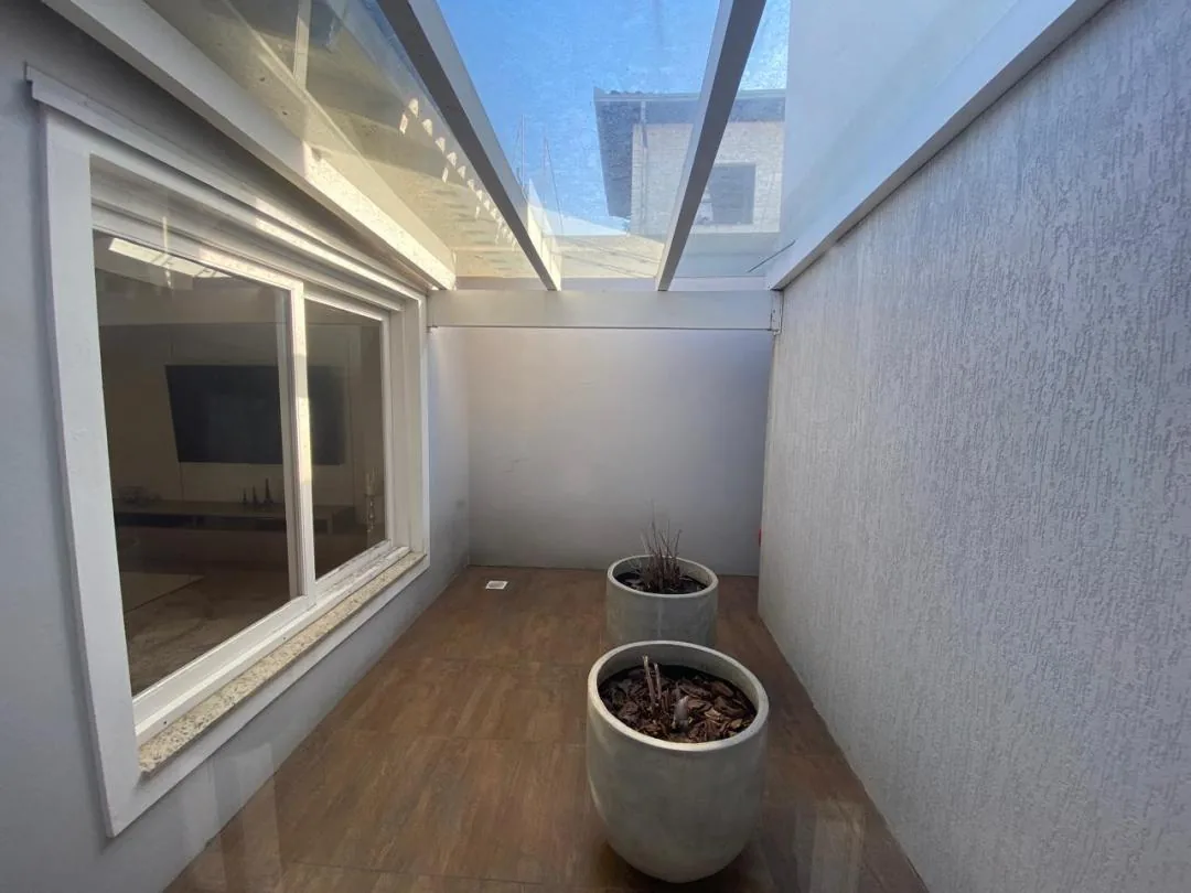 Pátio interno estreito com cobertura de vidro, dois vasos e janela ampla da sala