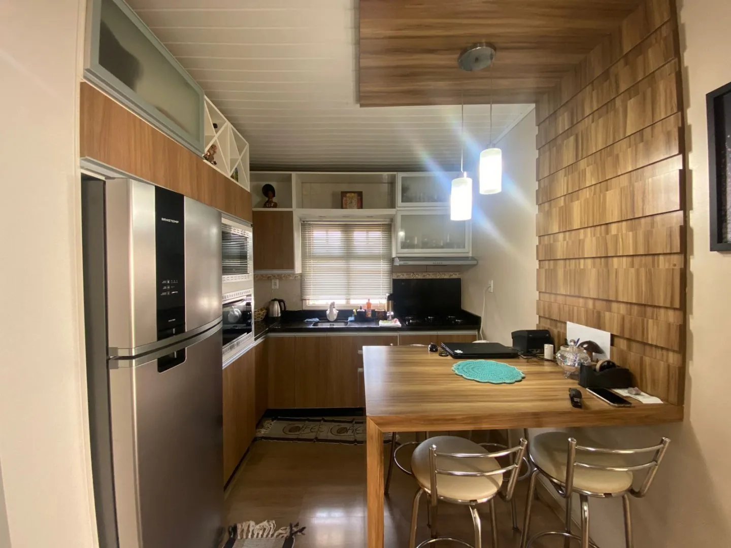 Cozinha planejada em madeira com geladeira inox, forno e micro-ondas embutidos e bancada de refeições com banquetas