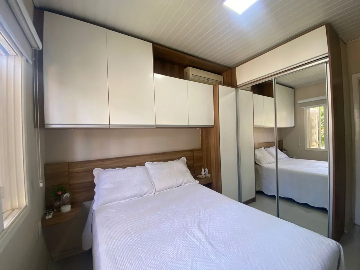 Dormitório de casal com armário planejado de portas brancas e guarda-roupa com porta de espelho