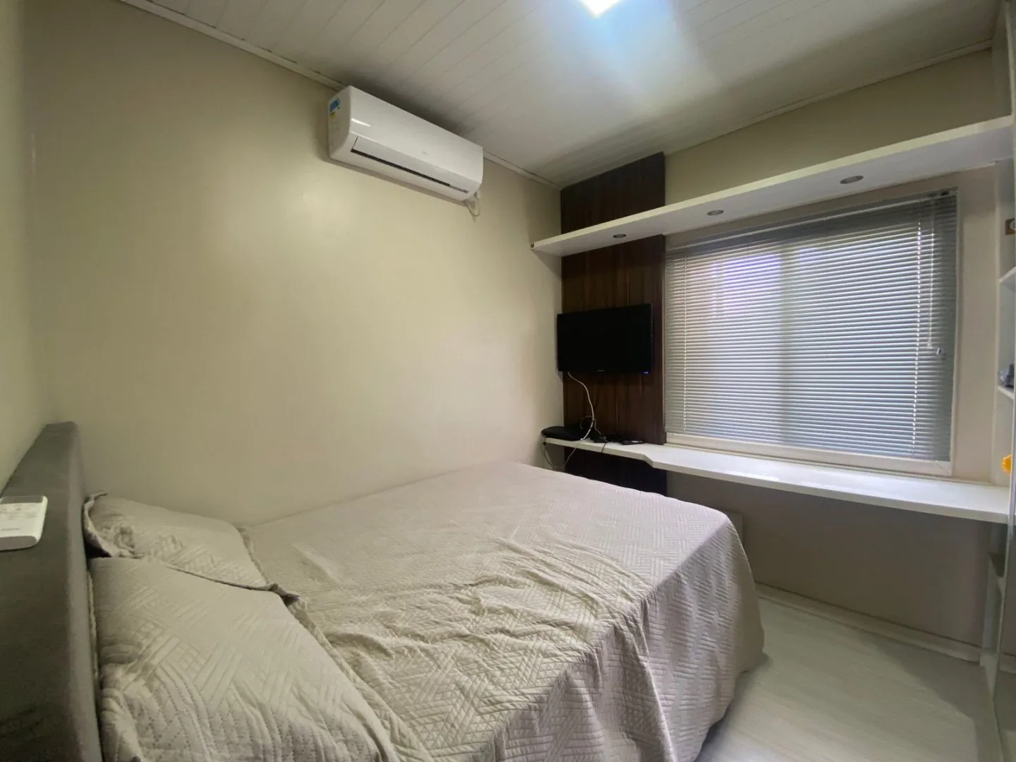 Segundo dormitório com ar-condicionado, bancada de estudo branca sob a janela com persiana e cama de casal