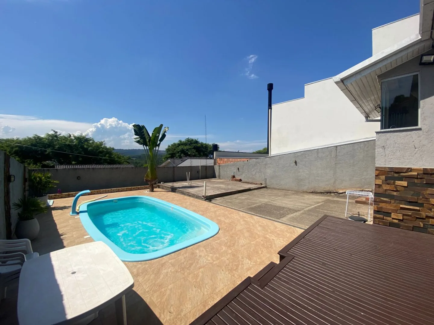Piscina de fibra com deck de madeira em primeiro plano e pátio murado com vegetação ao fundo