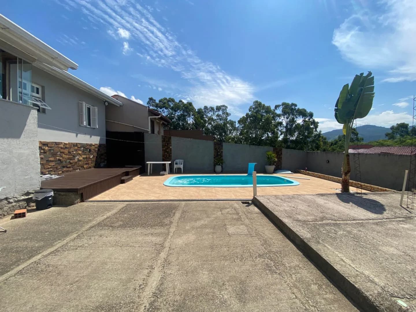 Pátio dos fundos amplo com piscina ao fundo, deck de madeira e muro com os morros no horizonte