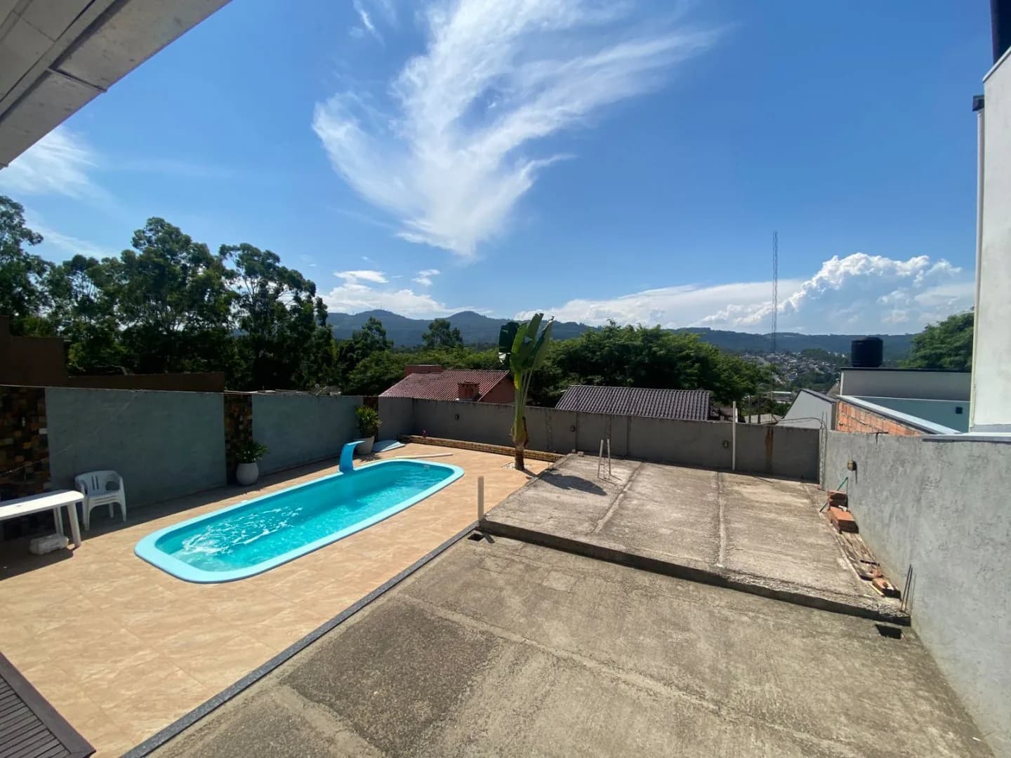 Piscina e pátio murado com morros e vegetação ao fundo sob céu azul