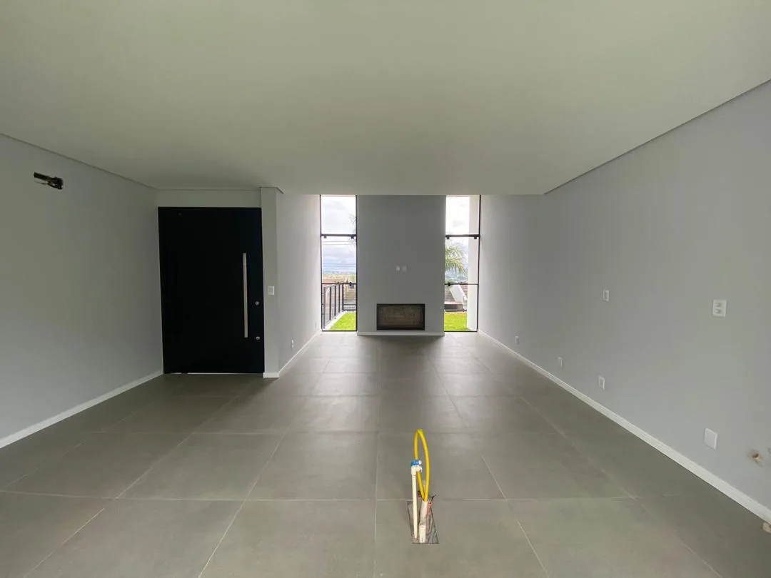 Living amplo com porcelanato cinza, porta de entrada preta à esquerda e lareira entre janelas altas ao fundo