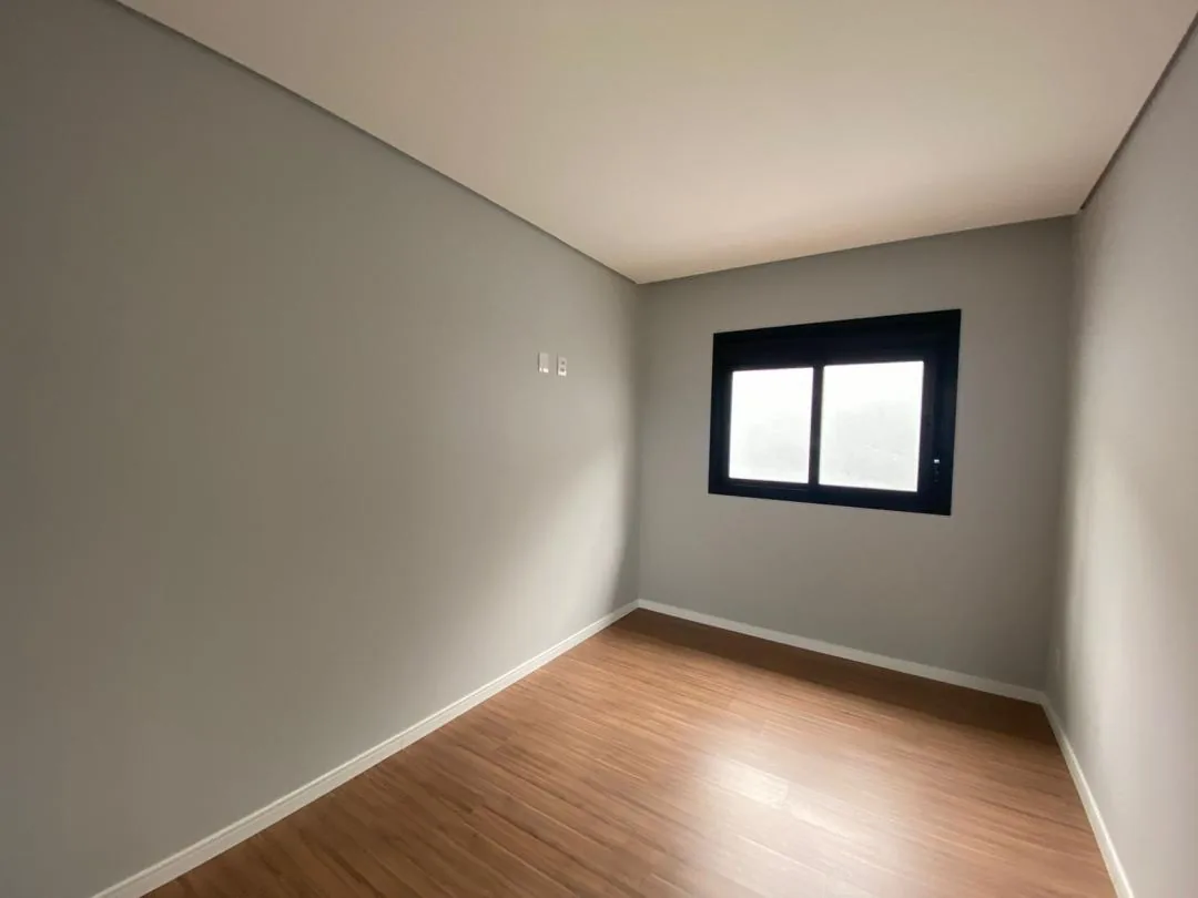 Dormitório com piso amadeirado, rodapé branco e janela de caixilho preto na parede do fundo
