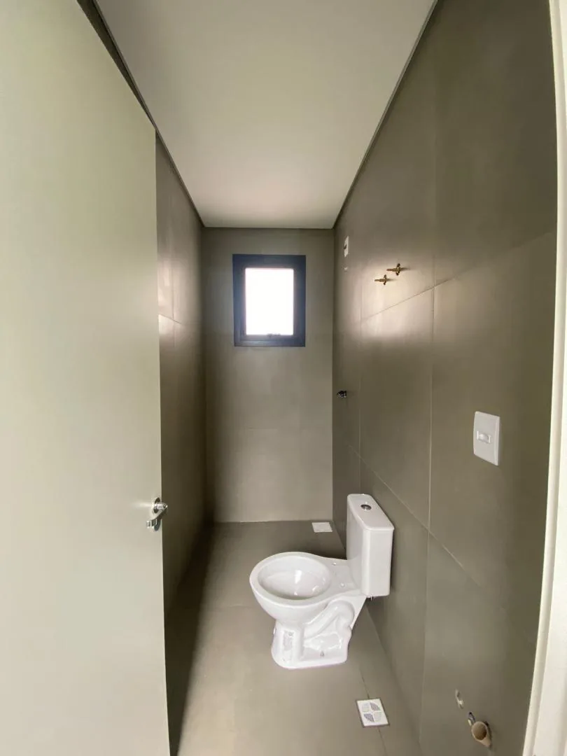 Banheiro com paredes em porcelanato cinza, vaso sanitário e janela pequena ao fundo