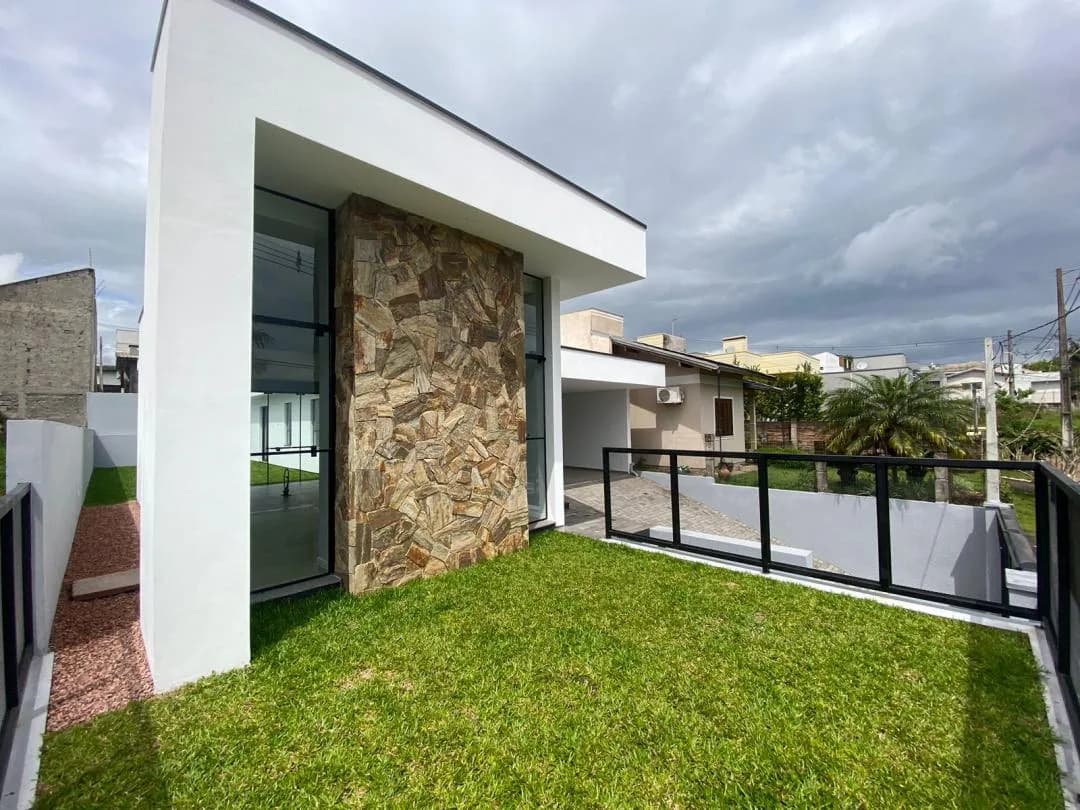 Lateral da fachada com pilar de pedra, vidros do piso ao teto e gramado cercado por guarda-corpo