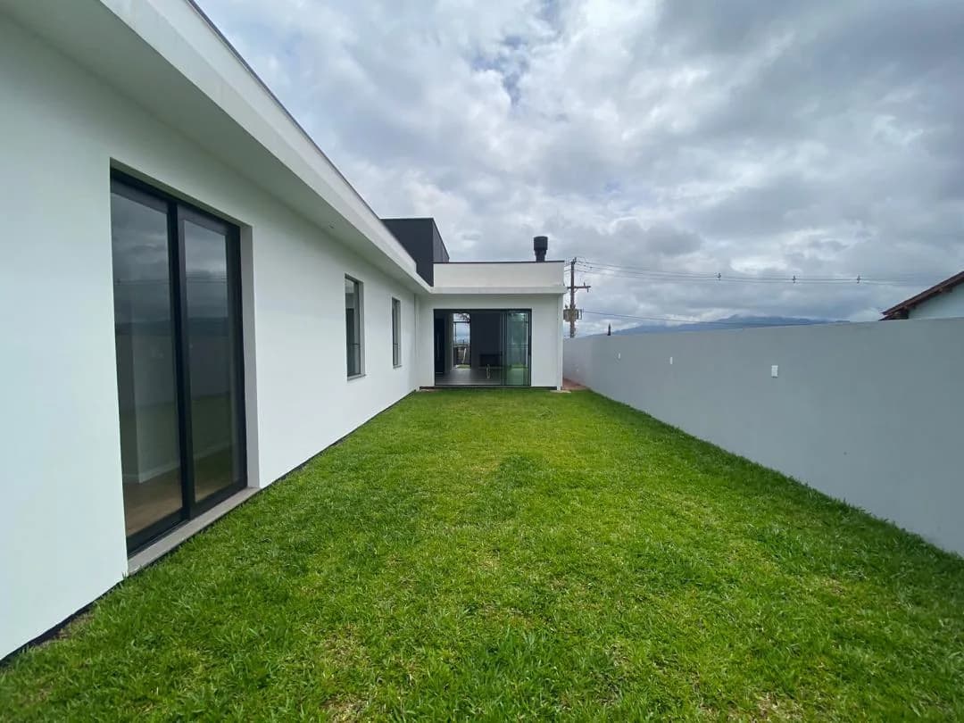 Pátio gramado dos fundos entre a lateral da casa, com porta de vidro, e o muro cinza