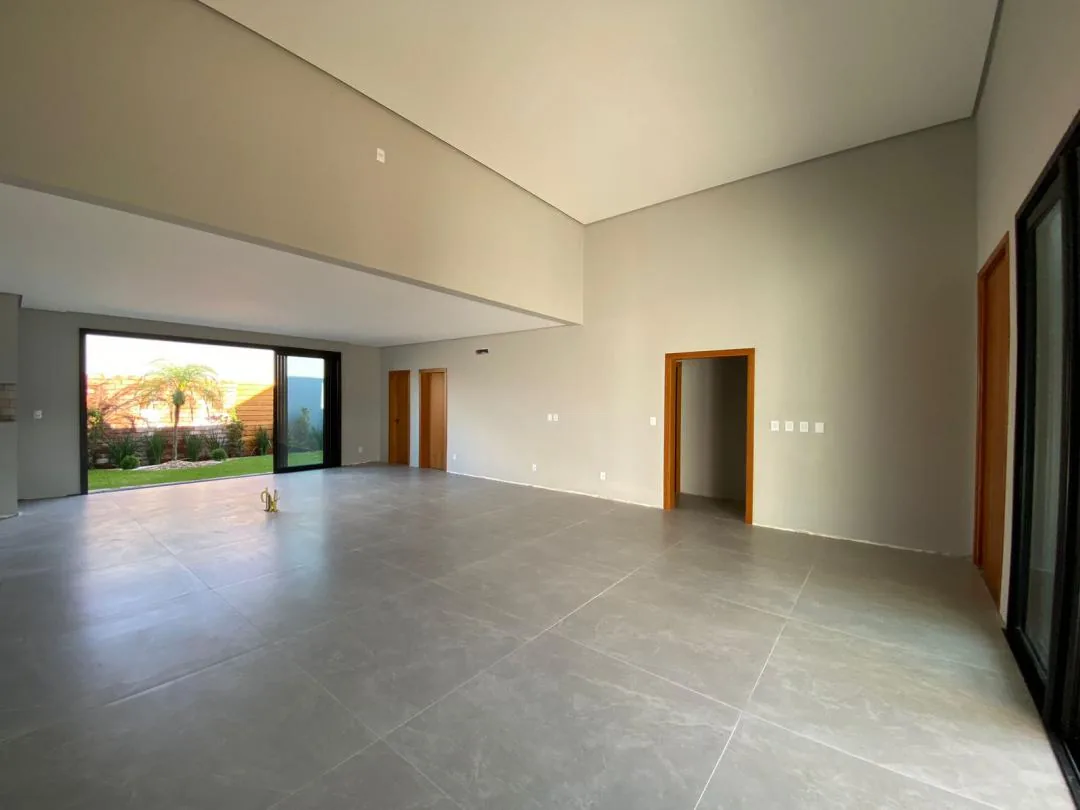 Sala integrada vazia com porcelanato cinza, portas de madeira e porta de vidro de correr aberta para o pátio com palmeira