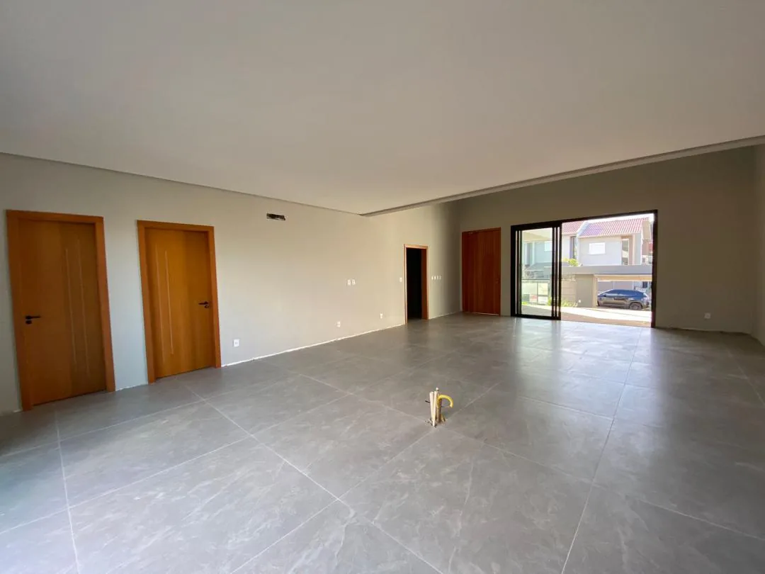 Sala vazia com duas portas de madeira à esquerda e porta de vidro de correr voltada para a frente da casa
