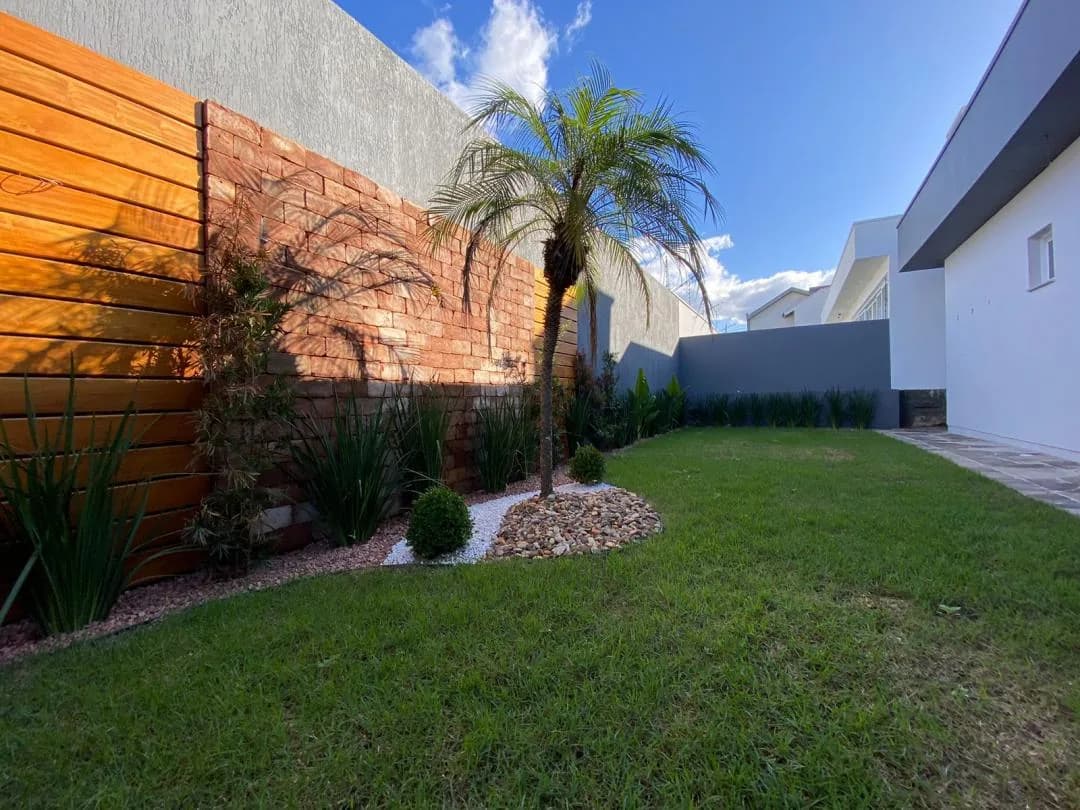 Canteiro com palmeira, arbustos e pedriscos junto ao muro de tijolos e ao painel de madeira do pátio