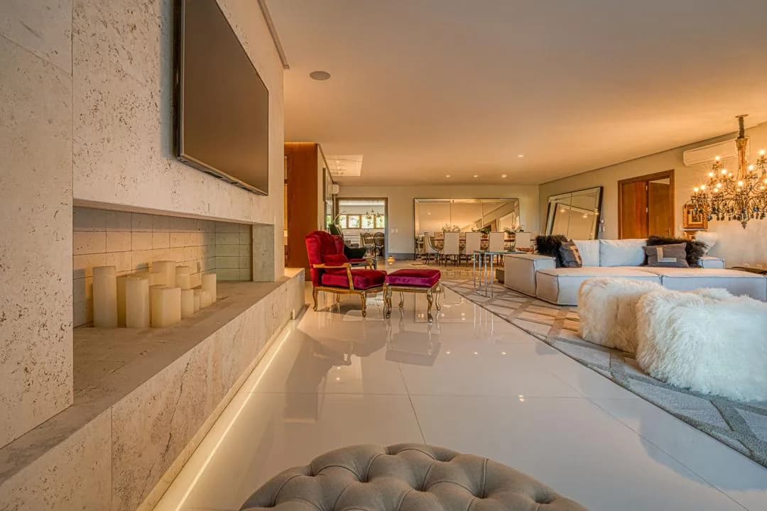 Living com parede revestida de pedra, TV embutida, nicho com velas e poltrona de veludo vermelho, com a sala de jantar ao fundo