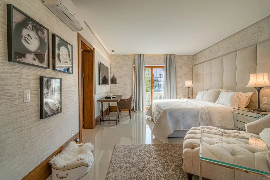 Suíte com parede de papel texturizado, quadros em preto e branco, escrivaninha e cama de casal com cabeceira estofada
