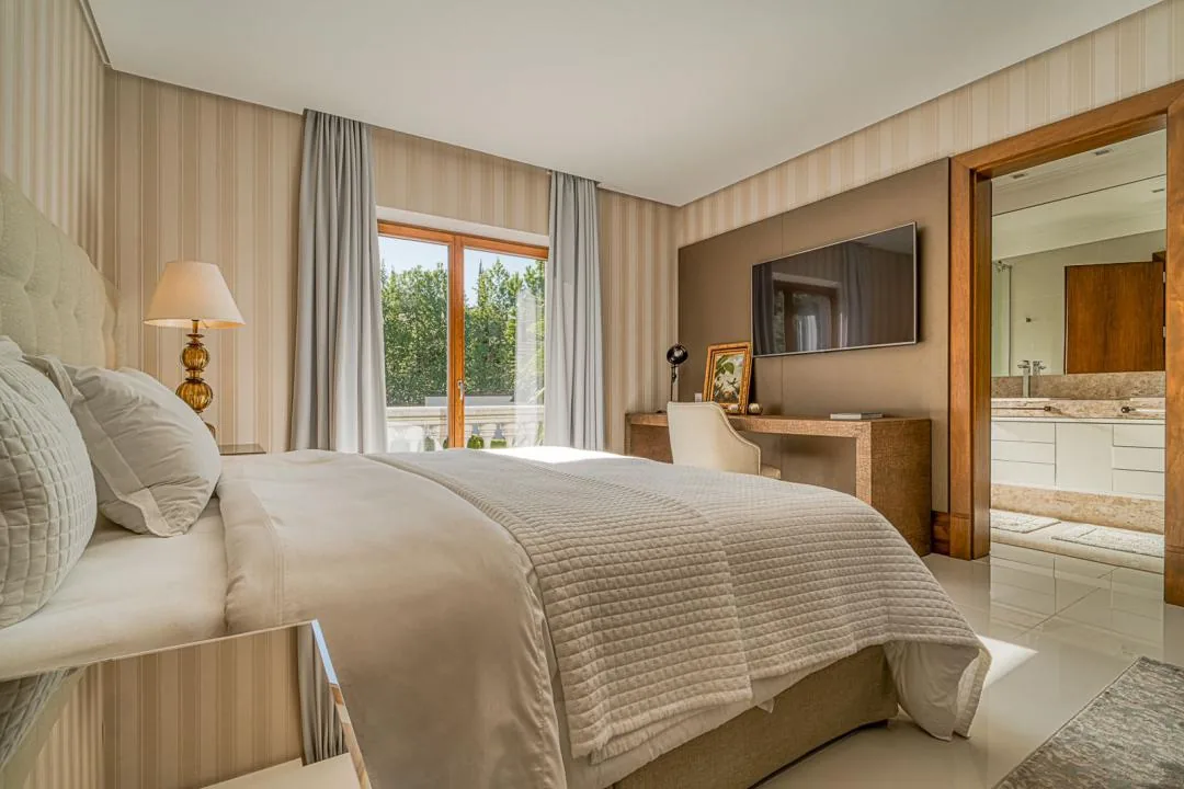 Suíte com cama de casal, TV na parede, escrivaninha e porta aberta para o banheiro