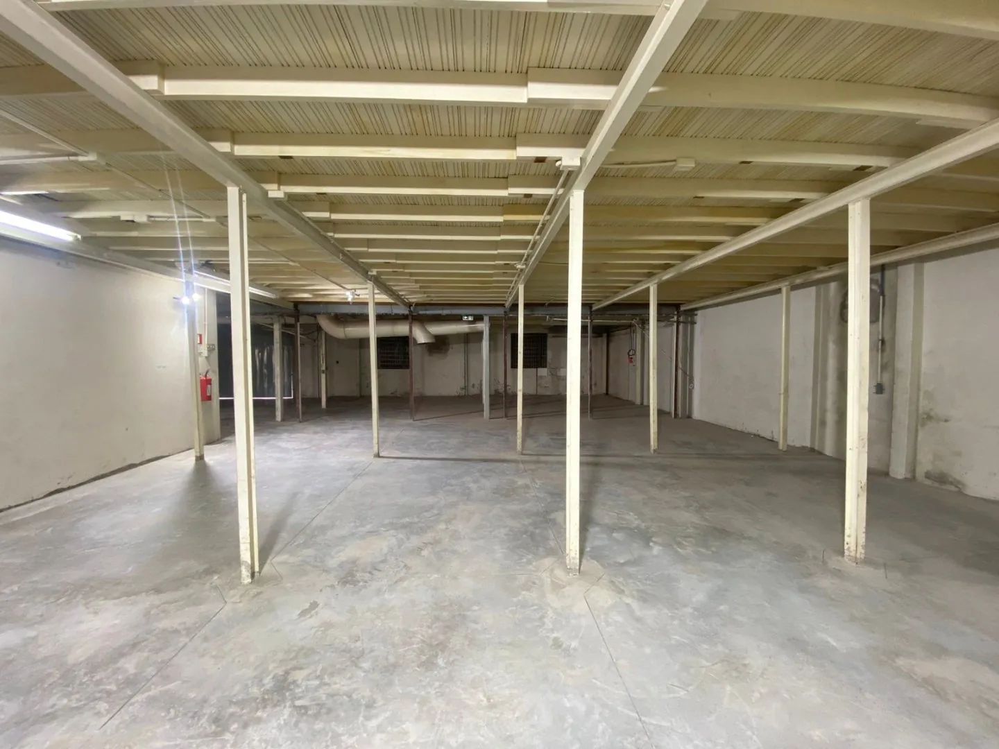 Área do térreo coberta pelo mezanino, com vigas e pilares brancos, paredes claras e piso de concreto