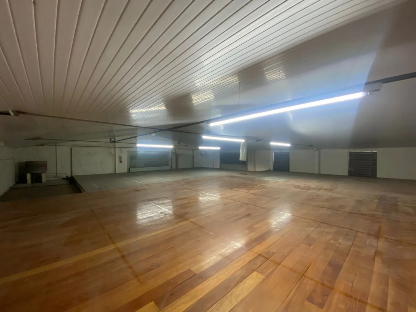 Mezanino com piso de tábuas de madeira, forro branco frisado e luminárias tubulares