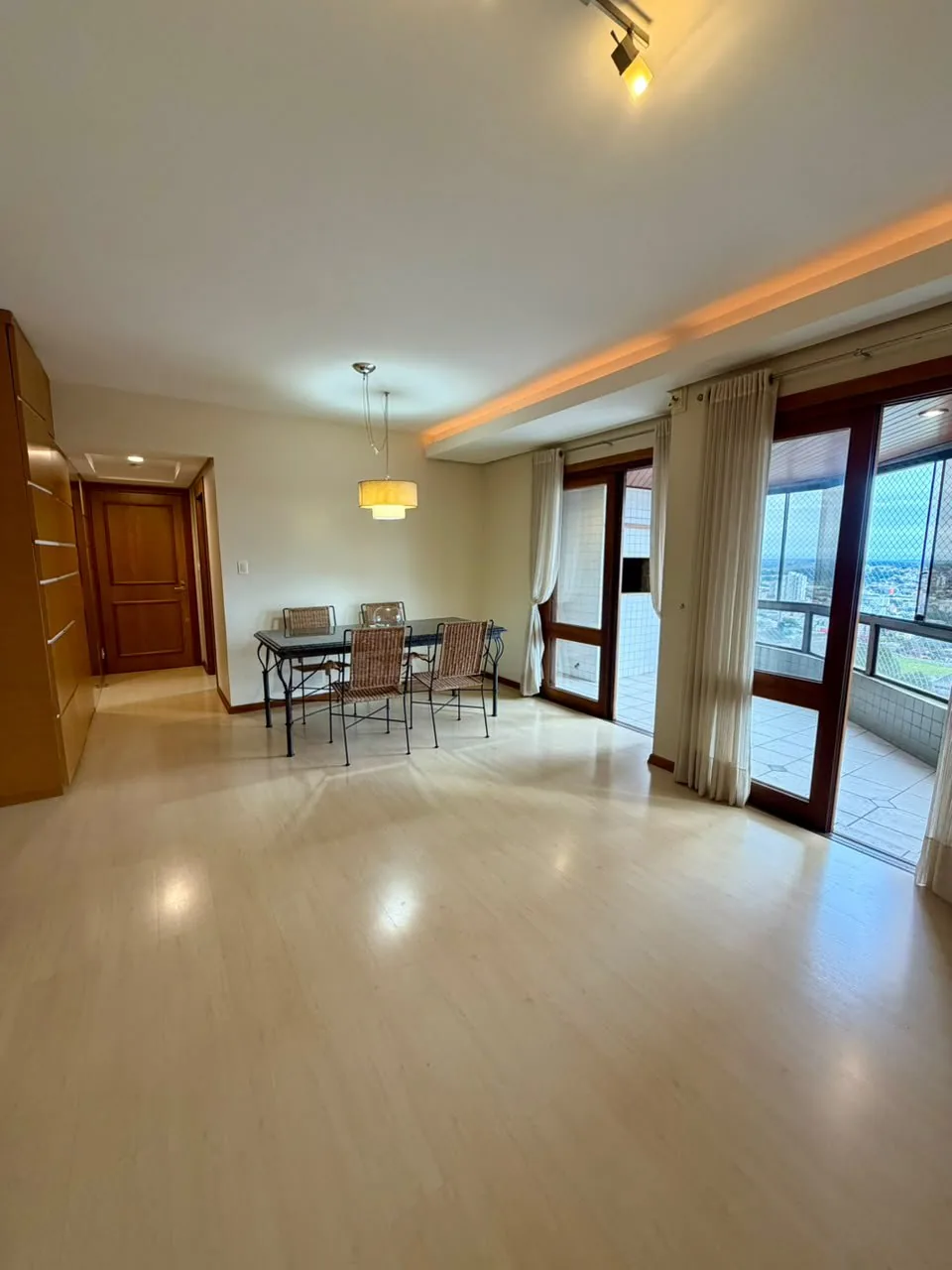Sala ampla com piso claro, sanca iluminada, mesa de jantar e portas de vidro abertas para a sacada envidraçada