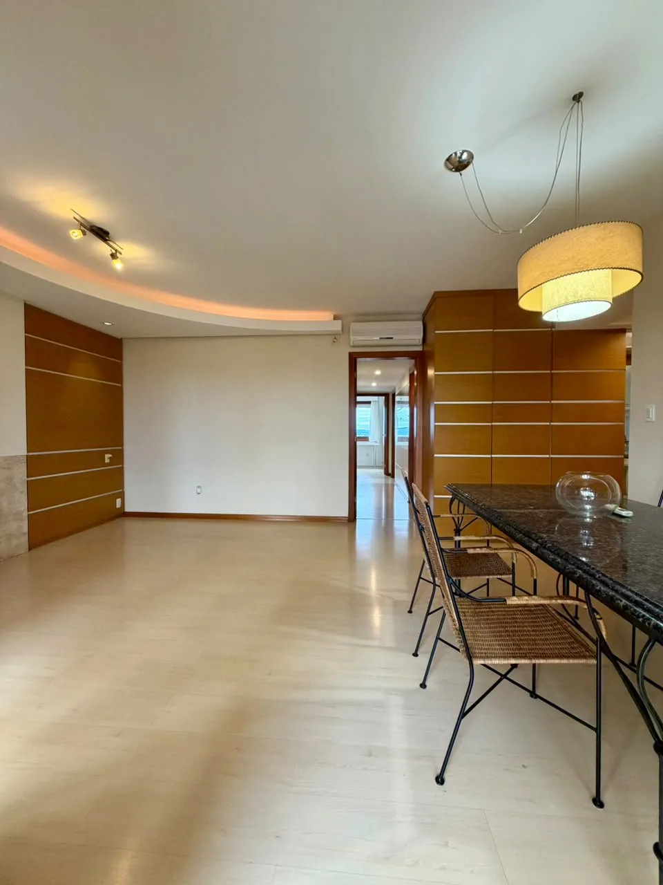 Sala com painéis de madeira frisados, luminária pendente sobre a mesa, ar-condicionado e porta para o corredor