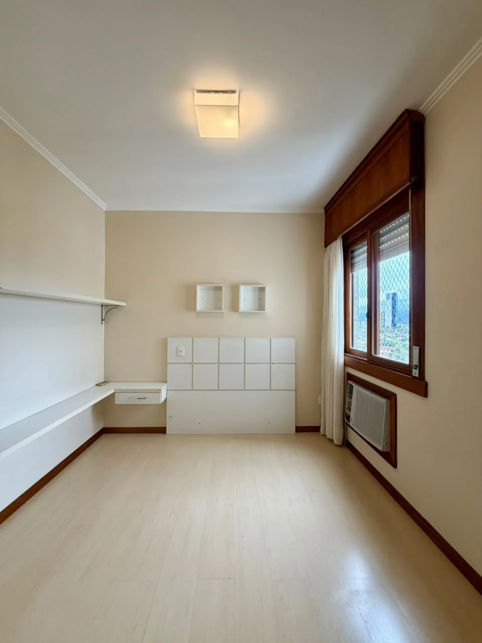 Quarto vazio com piso claro, cabeceira branca embutida, nichos na parede e ar-condicionado sob a janela