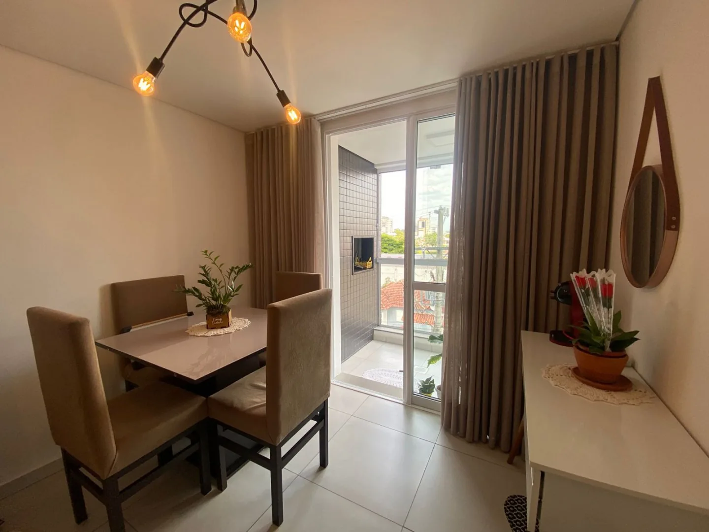 Sala de jantar com mesa de quatro cadeiras estofadas, cortinas até o chão e porta de vidro para a sacada