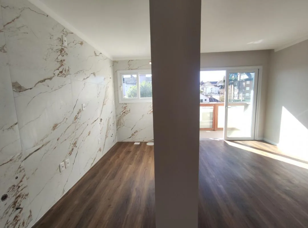 Cozinha com paredes em porcelanato marmorizado e janela, ao lado da sala com porta de vidro de correr para a sacada