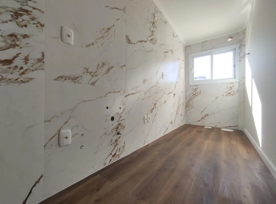 Cozinha ainda sem armários, com paredes em porcelanato branco de veios marrons, piso vinílico amadeirado e janela