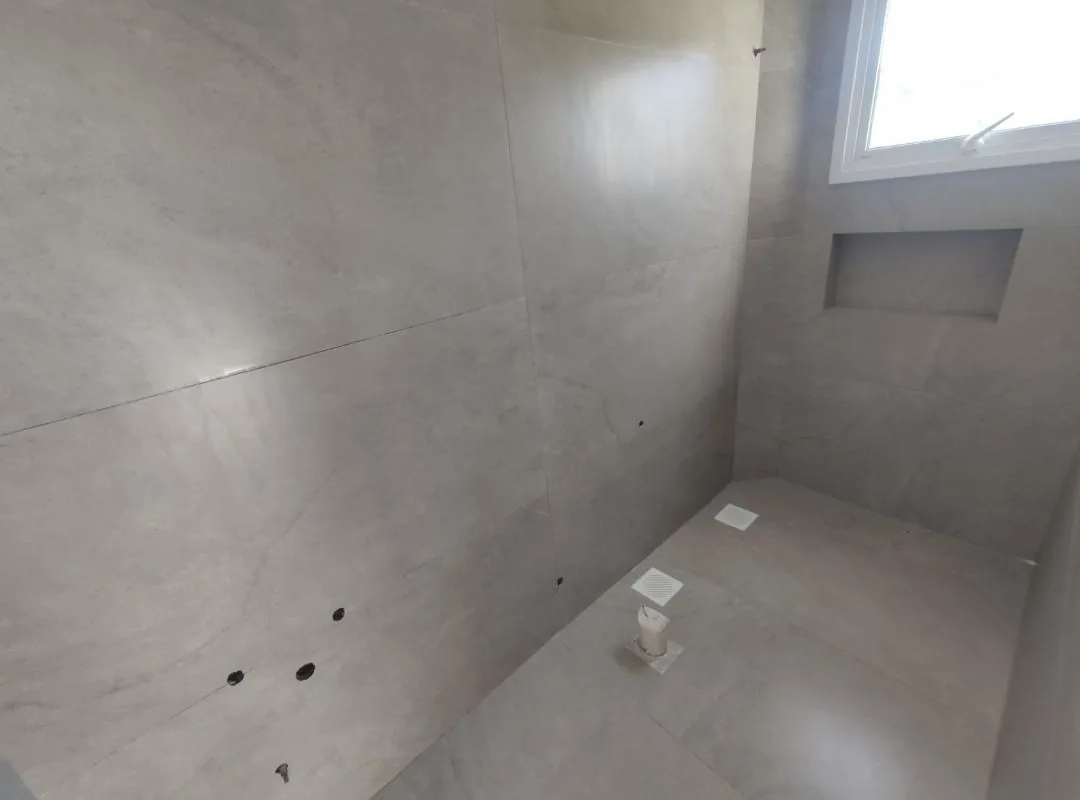 Banheiro revestido em porcelanato cinza, com nicho na parede e janela alta, ainda sem louças instaladas