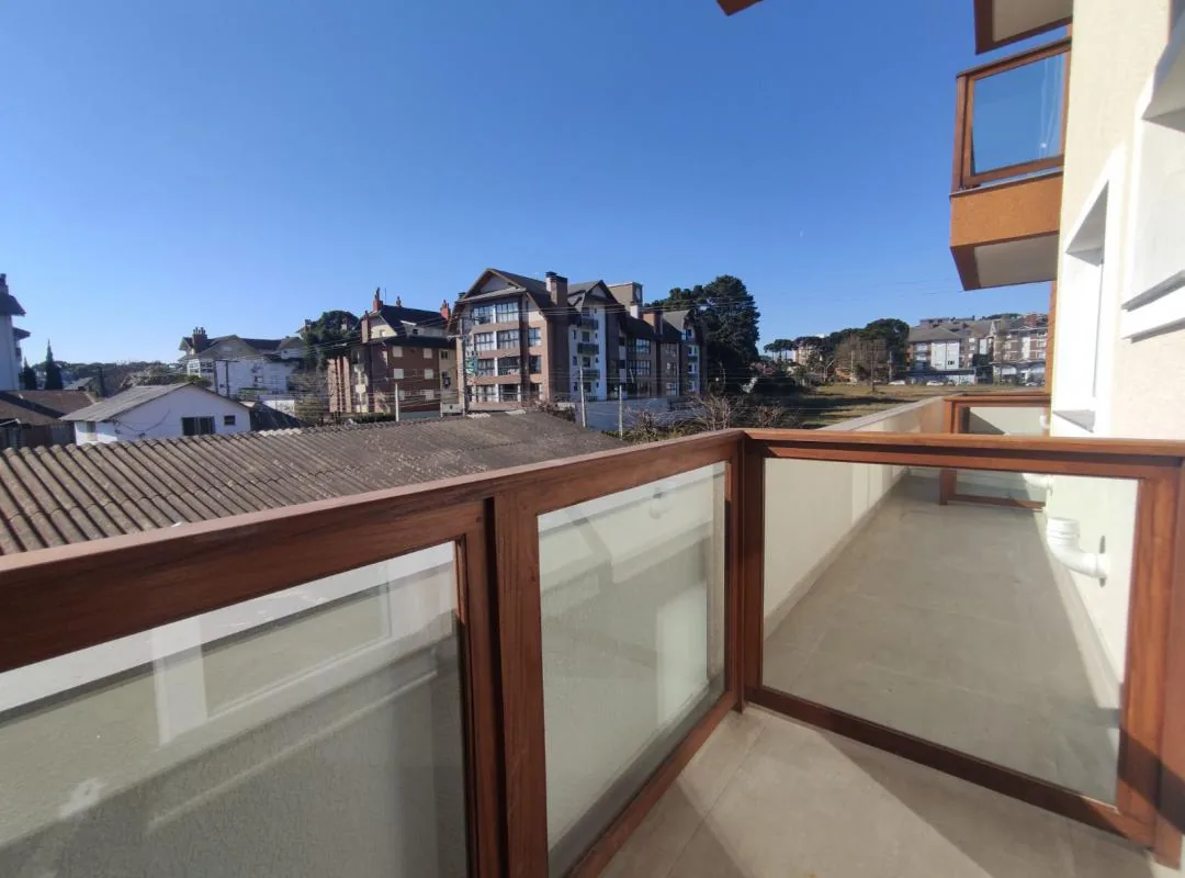 Sacada com guarda-corpo de madeira e vidro, piso claro e vista para os prédios vizinhos sob céu azul