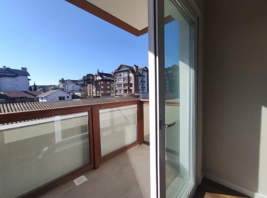 Porta de vidro de correr aberta para a sacada, com guarda-corpo de madeira e vidro e vista para os prédios vizinhos