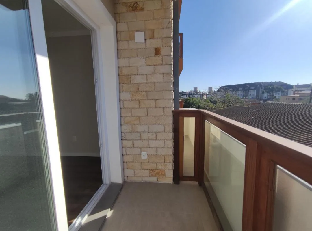 Sacada com parede de pedra, guarda-corpo de madeira e vidro e porta de correr que leva ao interior do apartamento
