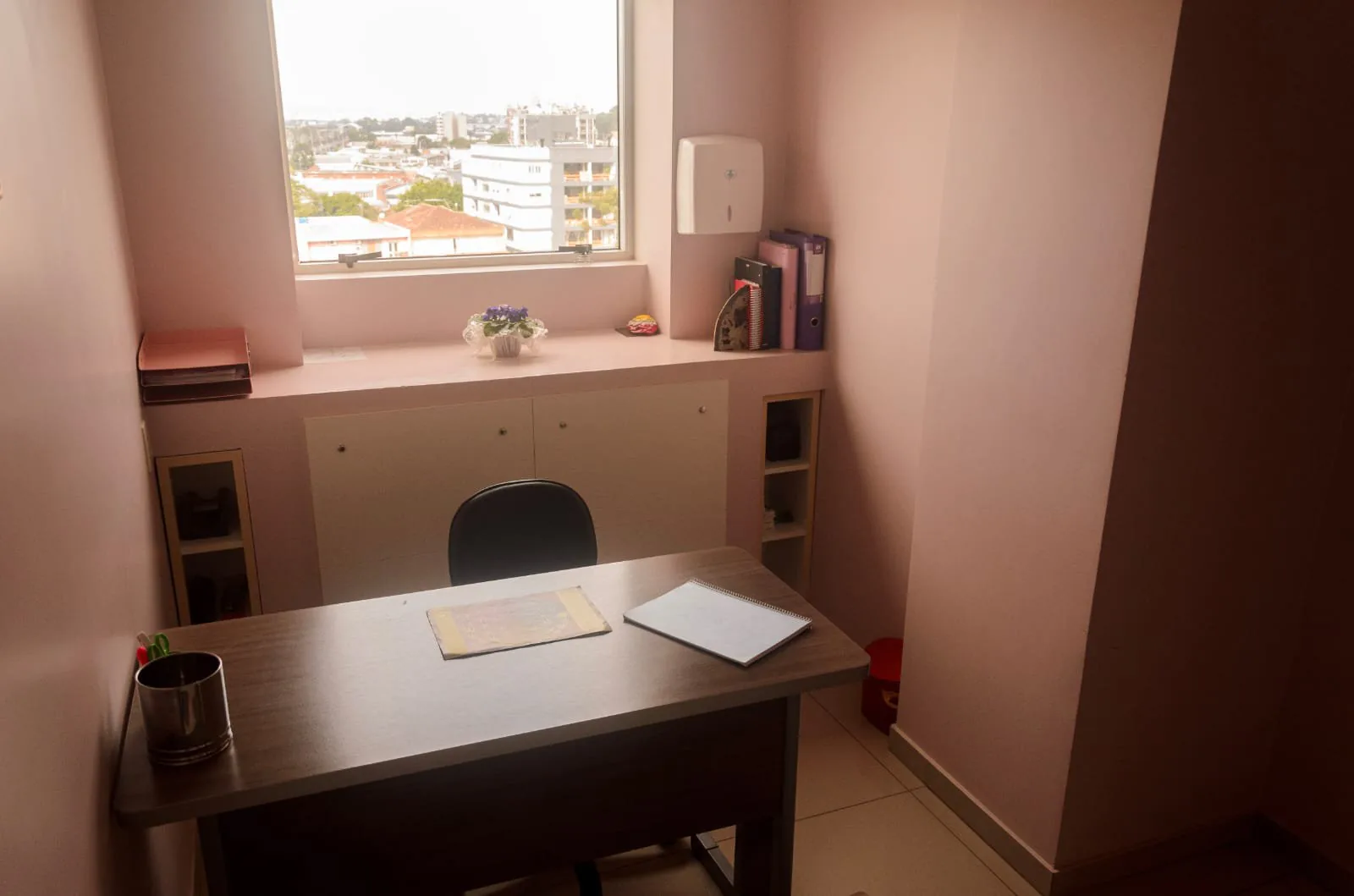 Sala com mesa de escritório, cadeira giratória e janela com vista para os prédios da cidade